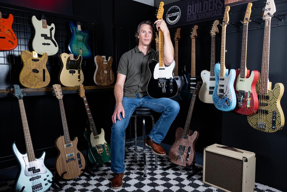 Man seated with electric guitars on display, showcasing various designs and colors.