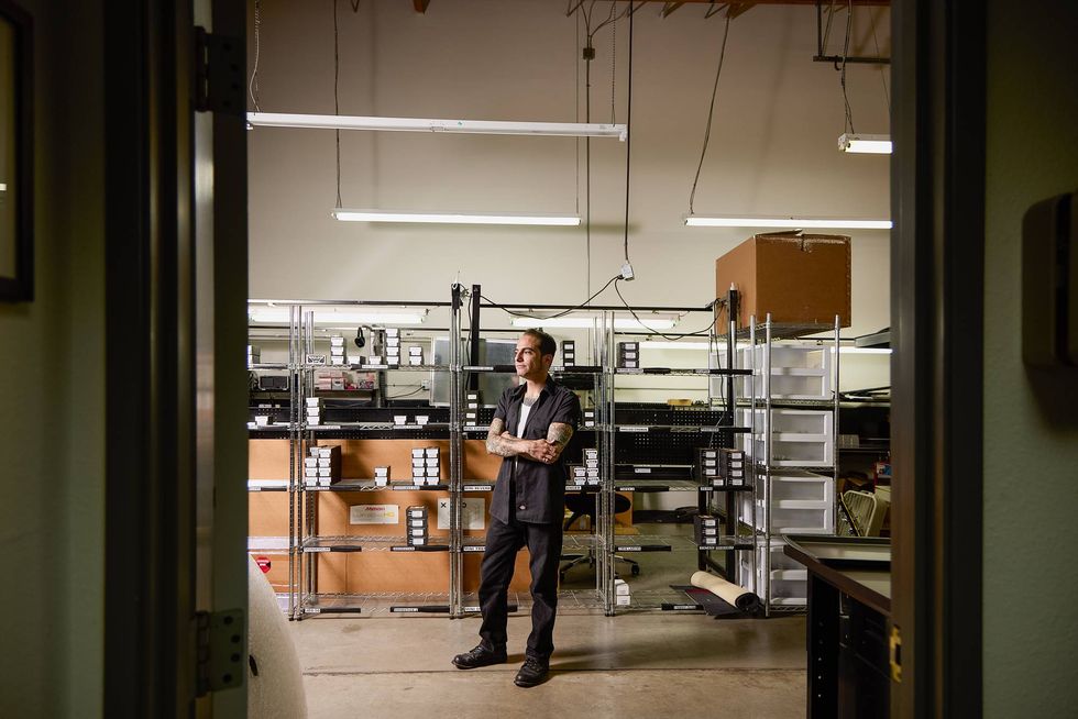 Man stands in a storage area with shelves filled with boxes and equipment.