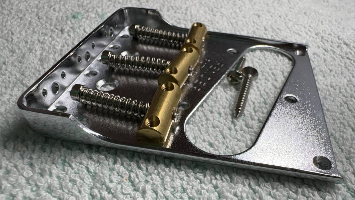 Metal guitar bridge plate with screws, featuring chrome finish and gold components.