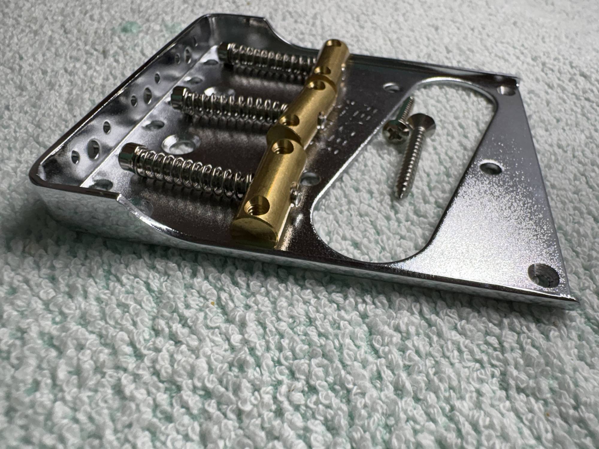Metal guitar bridge plate with screws, featuring chrome finish and gold components.