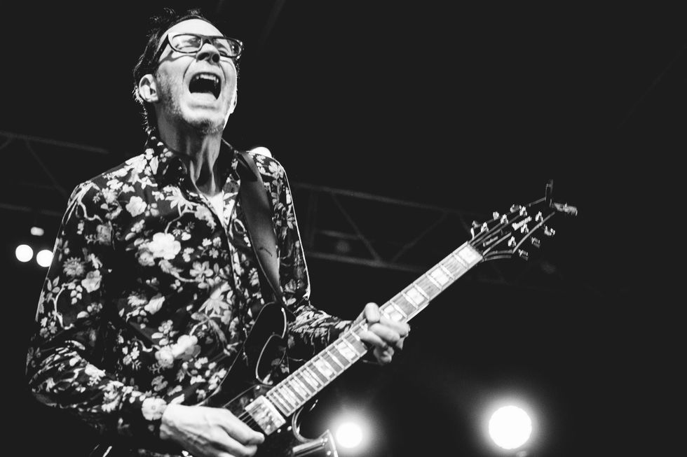 Musician in floral shirt passionately playing electric guitar on stage. Black and white.