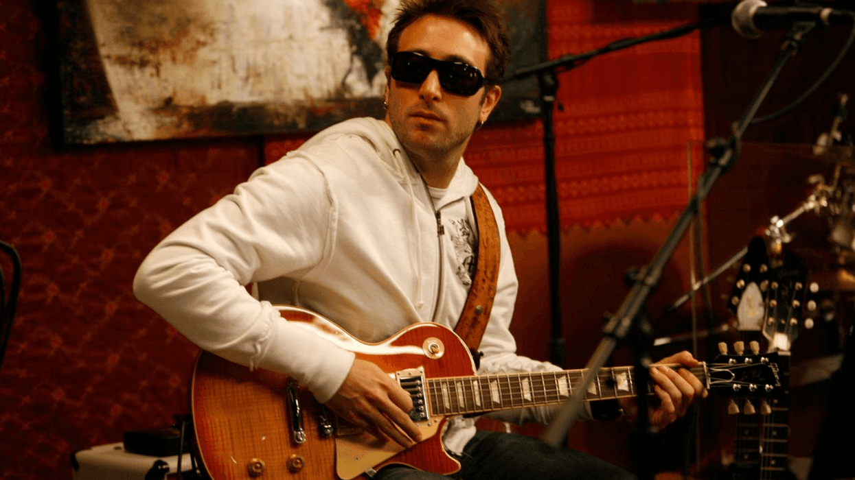 Musician in sunglasses plays an electric guitar in a cozy studio setting.