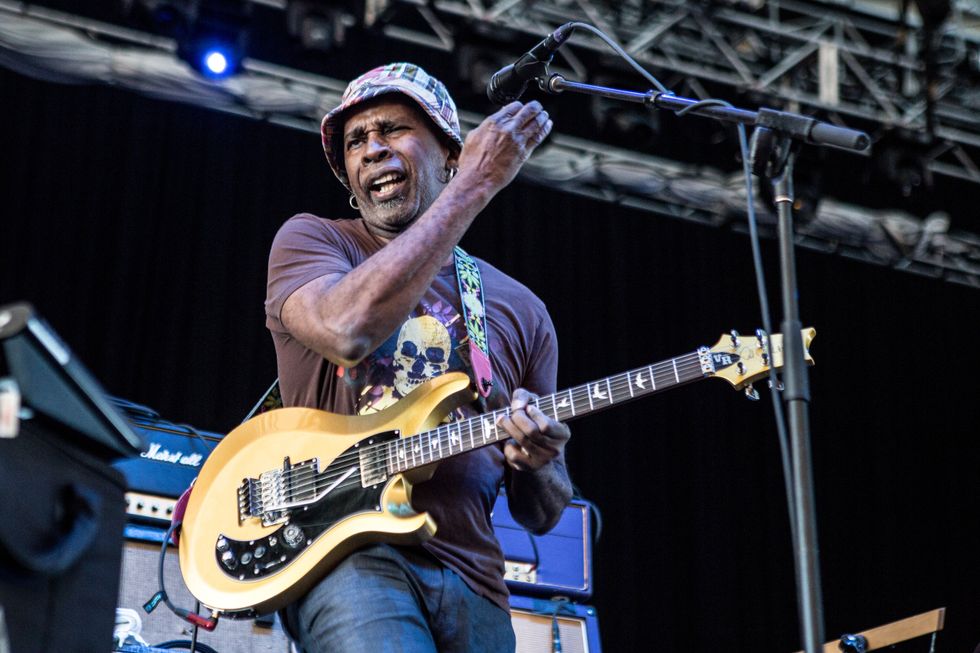 Musician passionately playing a yellow guitar on stage, microphone in front, vibrant atmosphere.