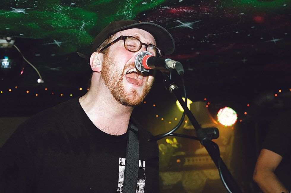 Musician passionately singing into a microphone, performing on stage under colorful lights.