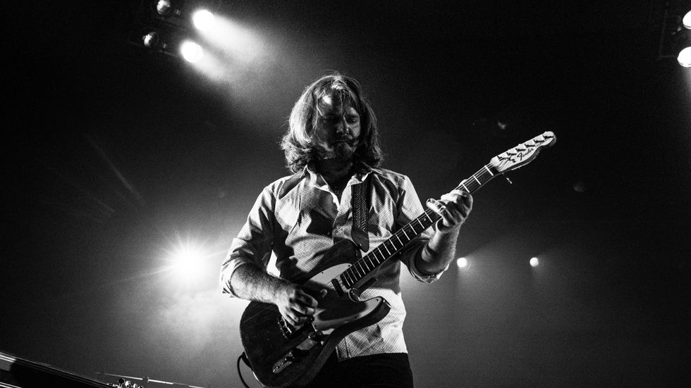 Musician playing an electric guitar on stage with dramatic lighting. Black and white photo.