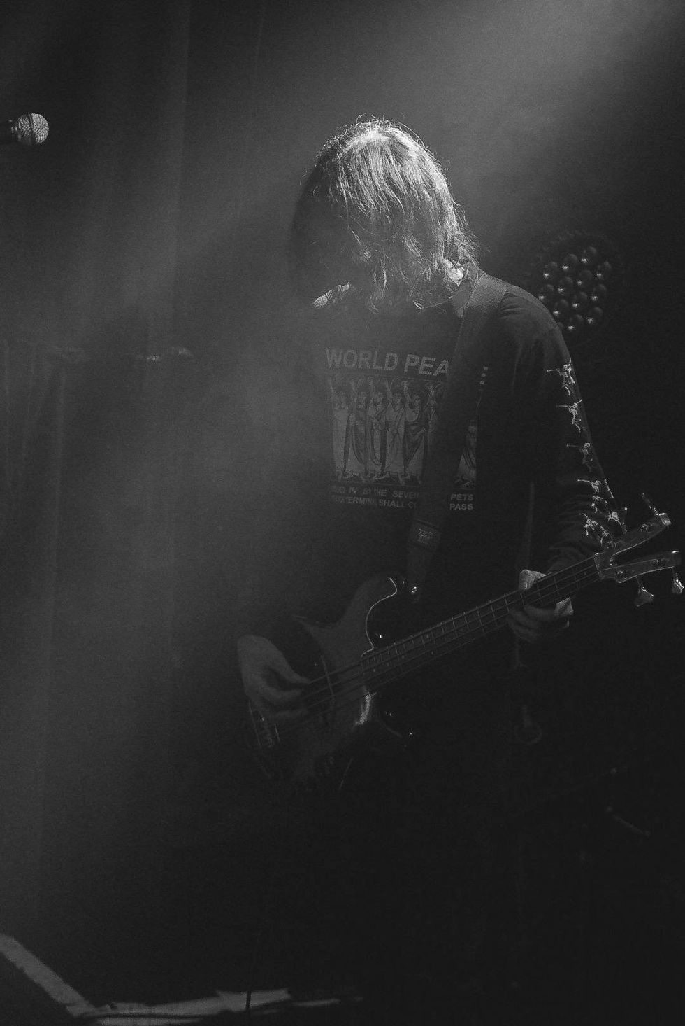 Musician playing bass guitar on stage, shrouded in smoke and dim lighting.