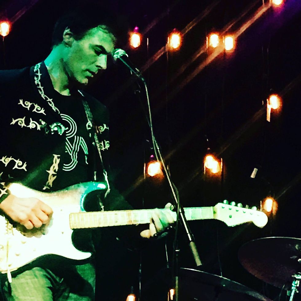 Musician playing electric guitar on stage with colorful lights in the background.