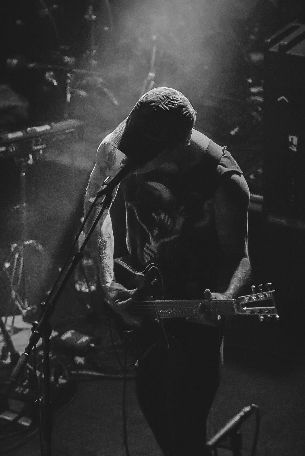 Musician playing guitar on stage, illuminated by dramatic lighting in a smoky atmosphere.