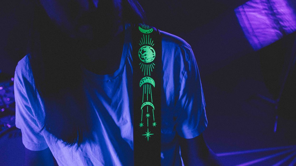 Musician wearing a glowing strap with celestial designs in low-light setting.