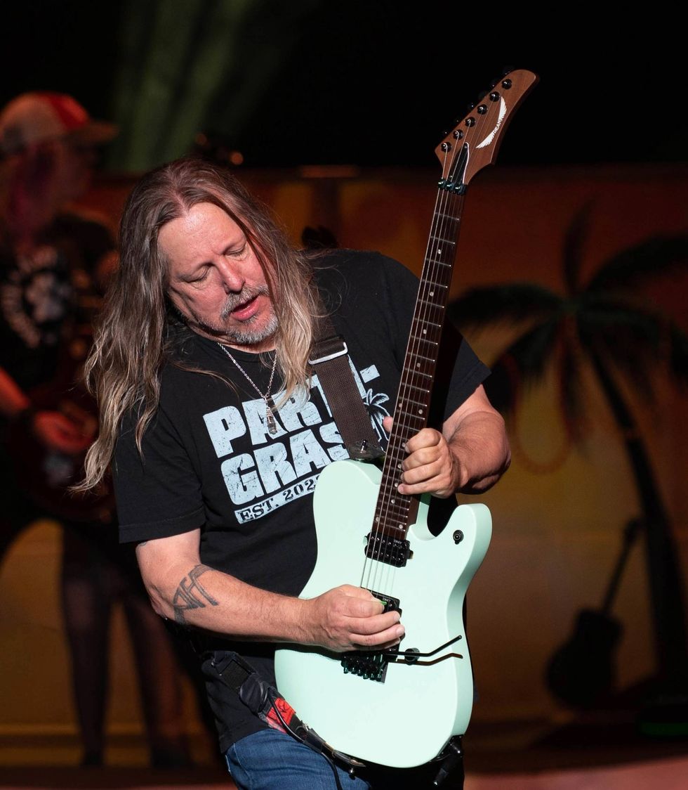 Musician with long hair passionately playing a mint green guitar on stage.