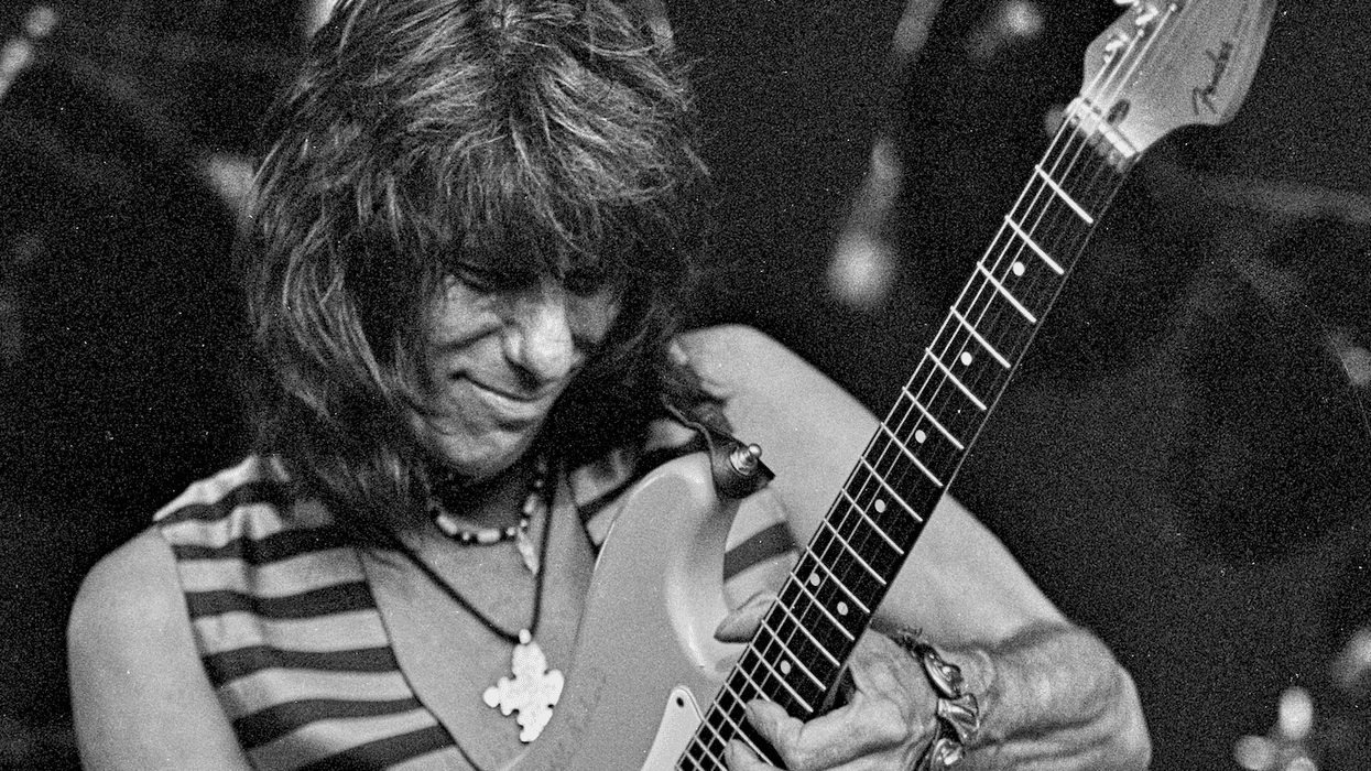 Musician with long hair plays an electric guitar passionately on stage.