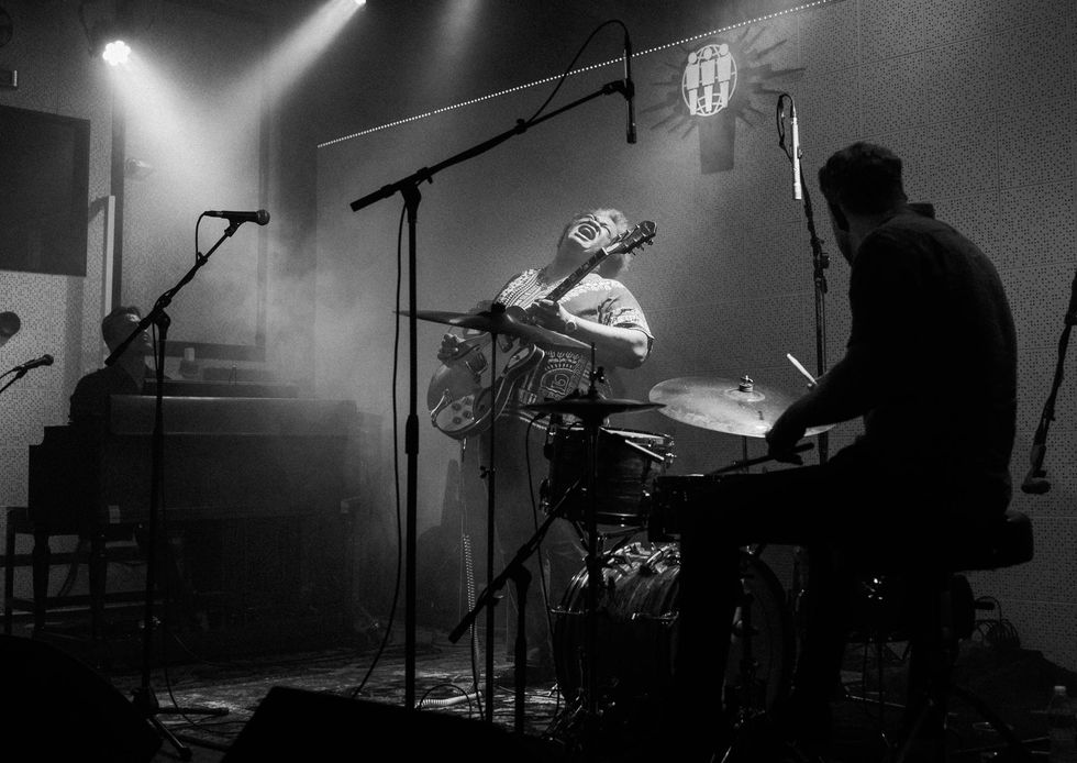 Musicians performing onstage, one singing passionately while playing guitar, with fog effects.