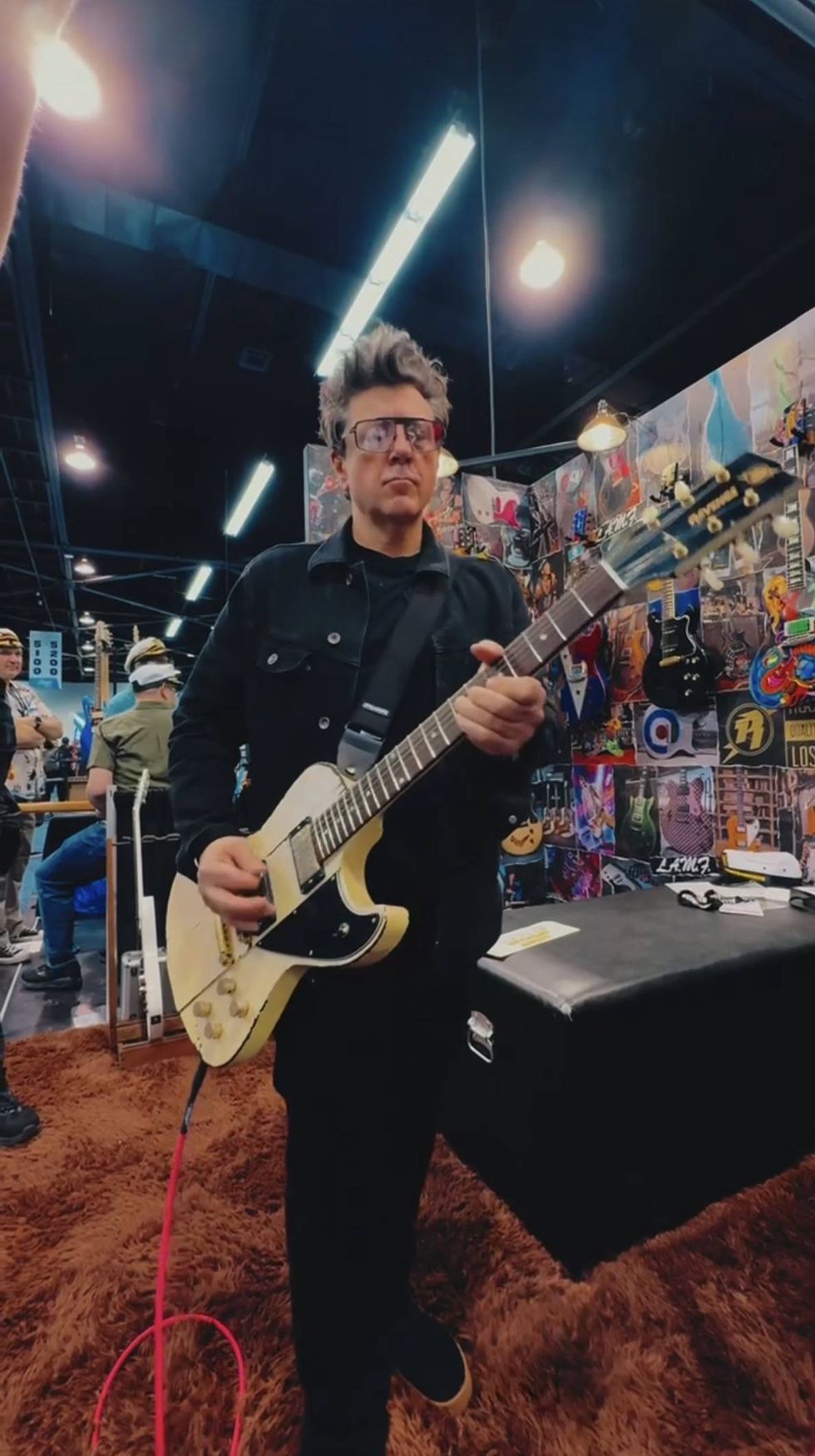 Person playing a white electric guitar in a music showcase with colorful backgrounds.