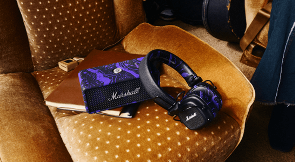 Purple and black Marshall headphones rest on a brown chair beside a notebook and speaker.