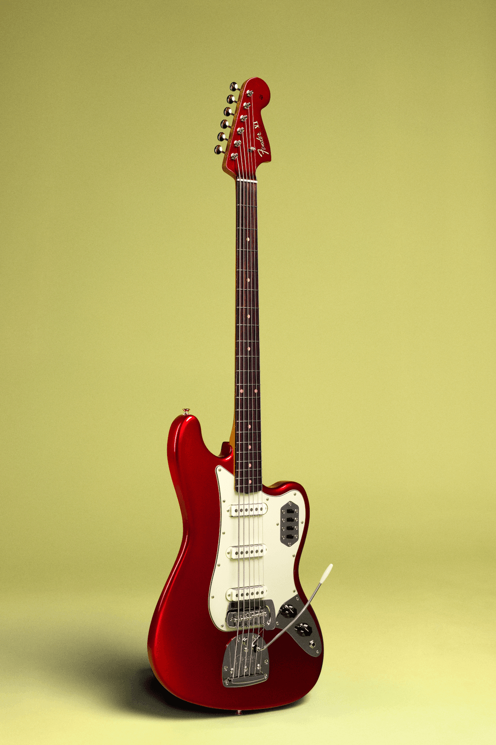 Red electric guitar with a curvy body and white pickguard set against a pale yellow background.