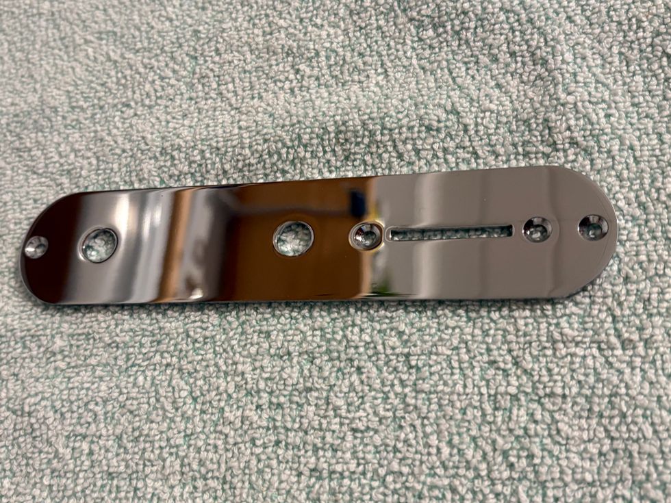 Shiny metal plate with three holes and a narrow slot, resting on a soft, textured surface.