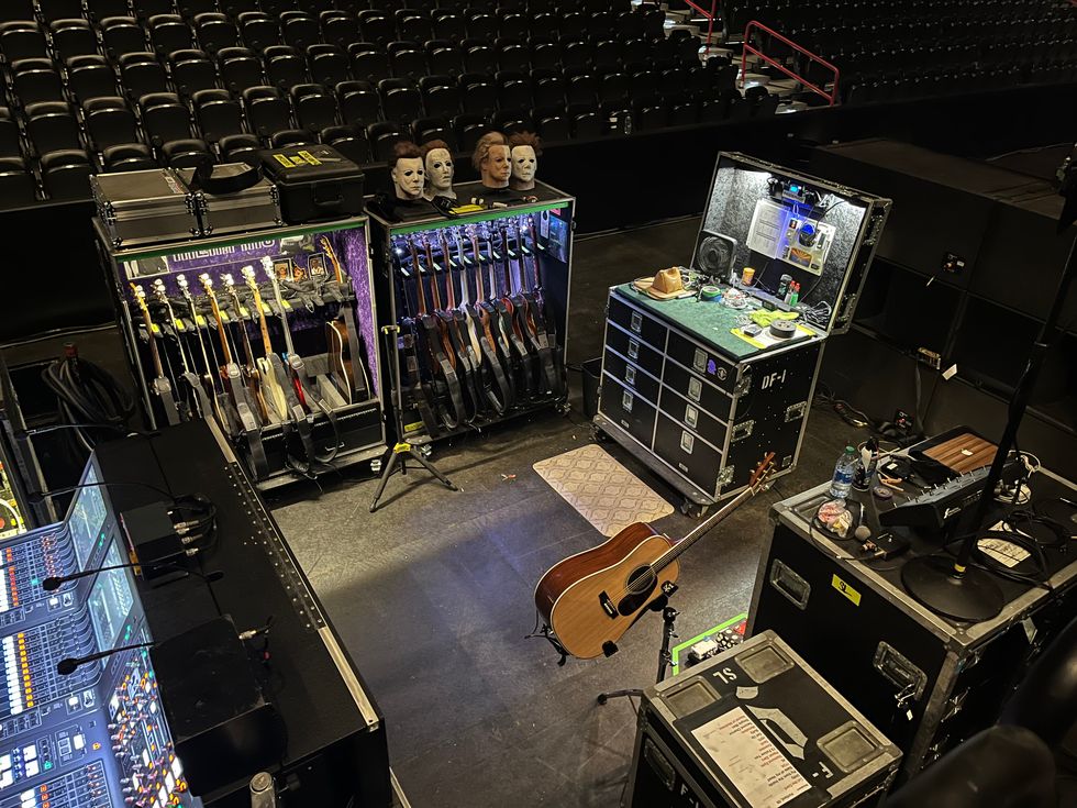Stage setup with guitars, equipment cases, and masks against empty seating.