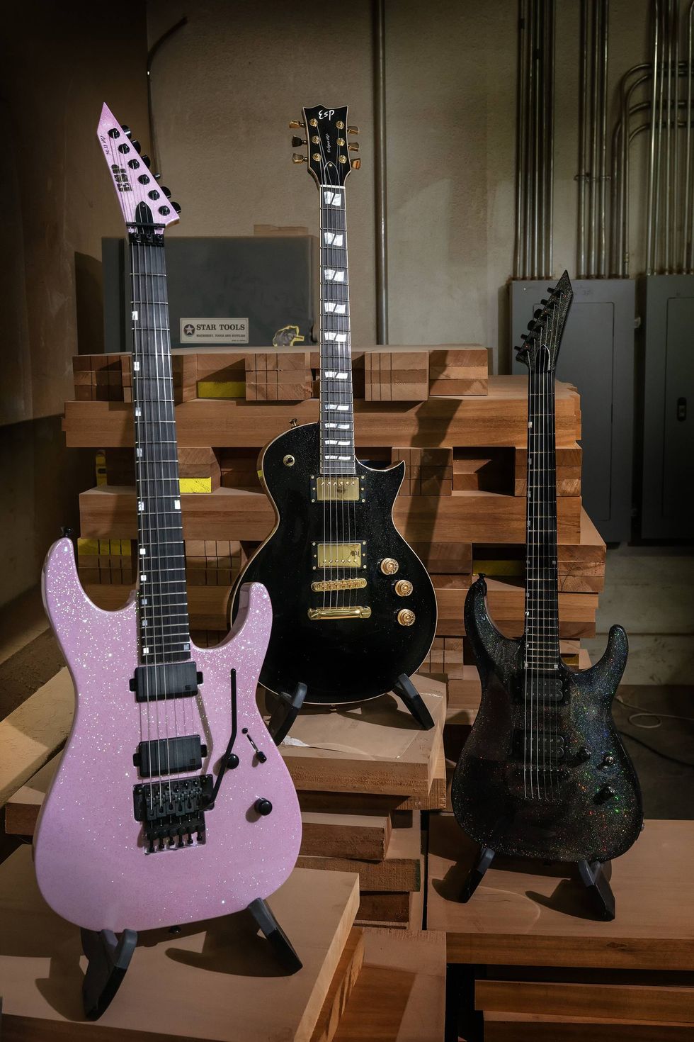 Three electric guitars in various colors displayed on wooden podiums in a workshop.