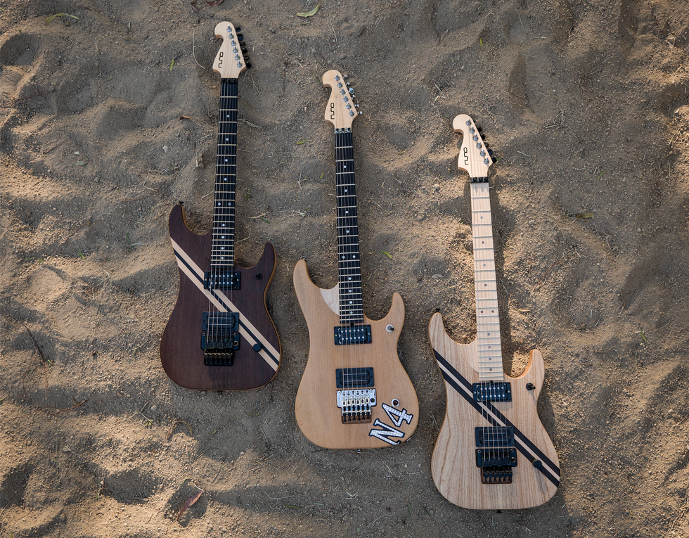 Three electric guitars placed on sandy ground, showcasing varying wood finishes and designs.