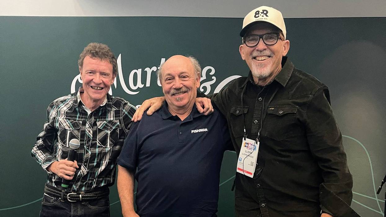 Three smiling men stand together, each holding a microphone, in front of a green backdrop.
