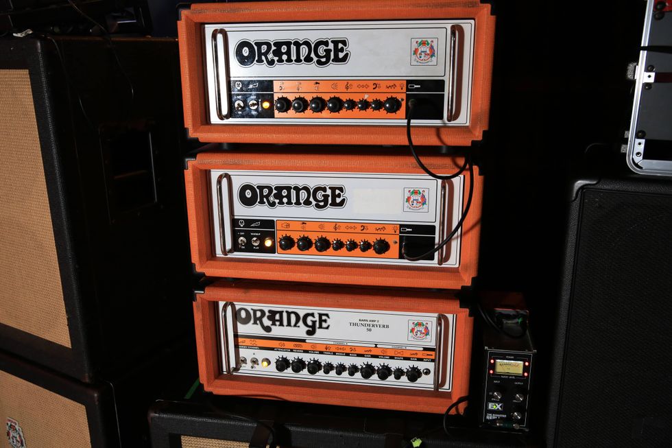 Three stacked Orange guitar amplifiers with various controls, on a dark stage background.