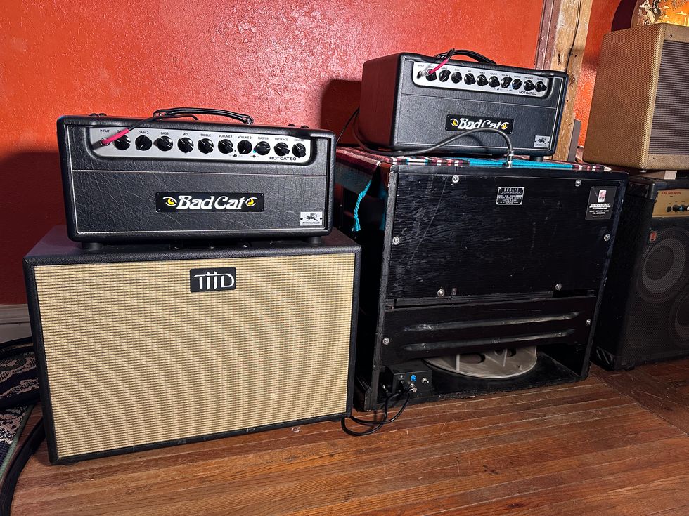Two Bad Cat guitar amplifiers on top of a speaker cabinet, set against a red wall.