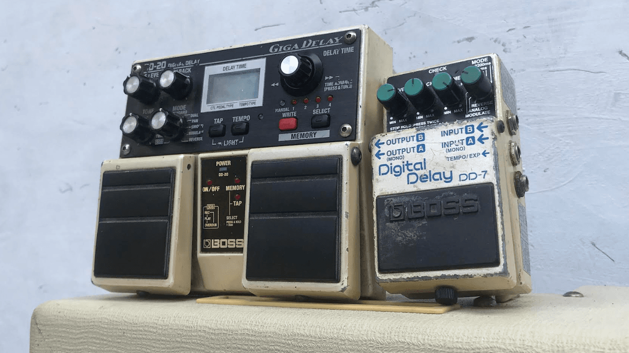 Two Boss guitar delay pedals stacked on a vintage amplifier against a plain wall.