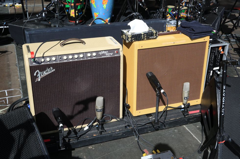 Two Fender guitar amplifiers on a stage with microphones and musical equipment in the background.