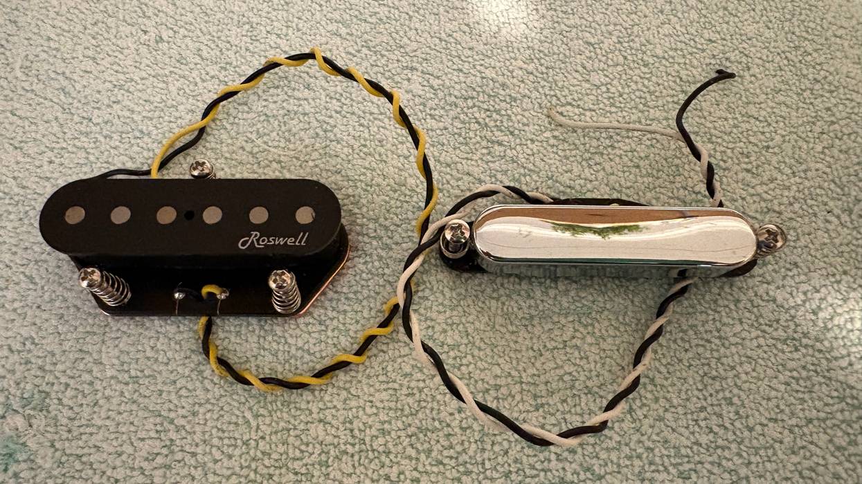 Two guitar pickups on a textured surface: one black with wires, one shiny silver with attached wires.