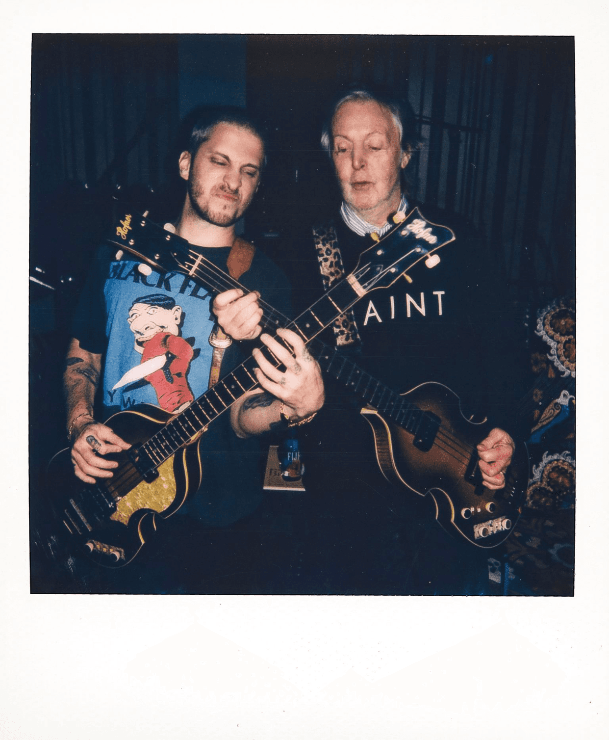 Two guitarists performing together, one in a graphic T-shirt and the other in a stylish sweater.
