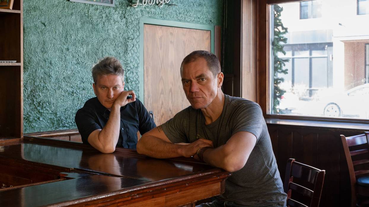 Two men seated at a bar, deep in thought, with a green wall and windows in the background.