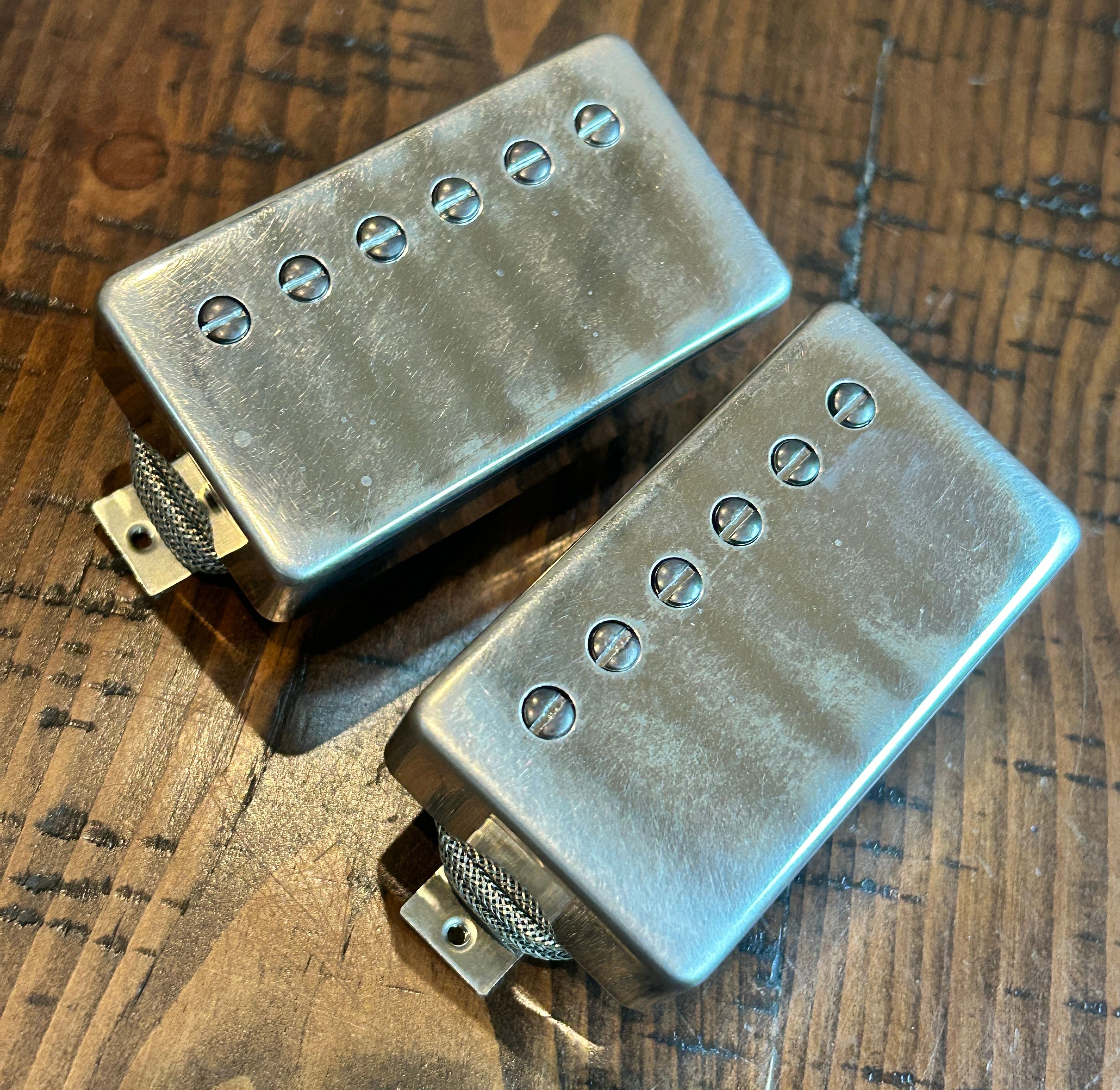 Two metal guitar pickups on a wooden surface, showcasing their sleek, brushed finish.