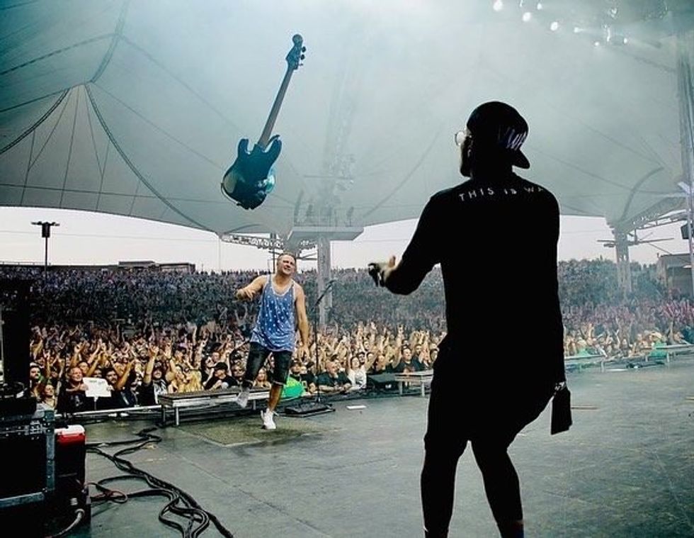 Two musicians perform on stage, with an enthusiastic crowd and a flying guitar above.