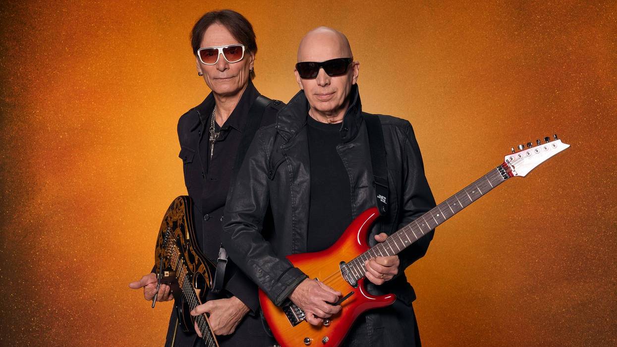 Two musicians pose confidently with electric guitars against an orange background.
