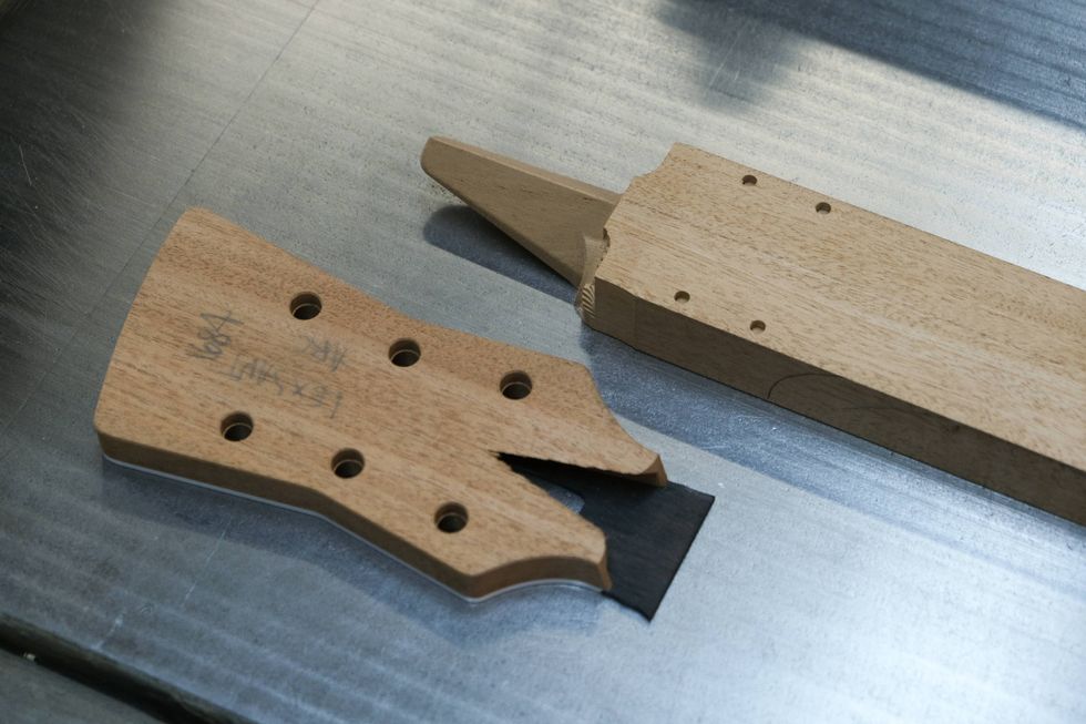 Two wooden guitar neck components laid on a metallic surface, showcasing their unfinished state.
