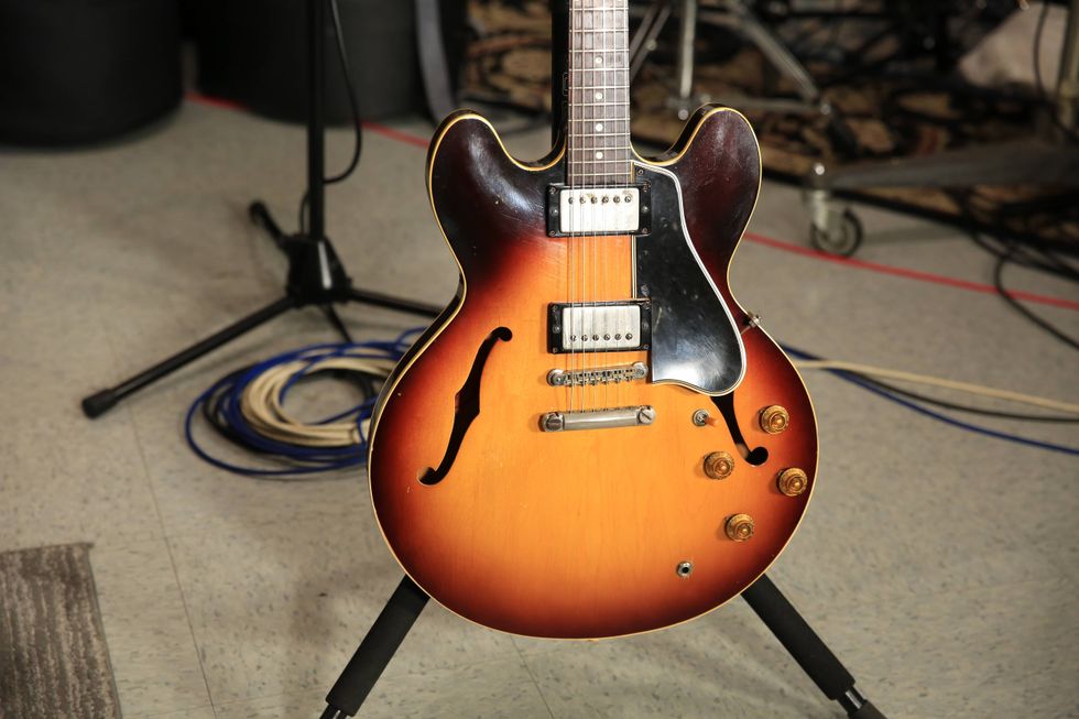 Vintage sunburst electric guitar on a stand, with cables in the background.