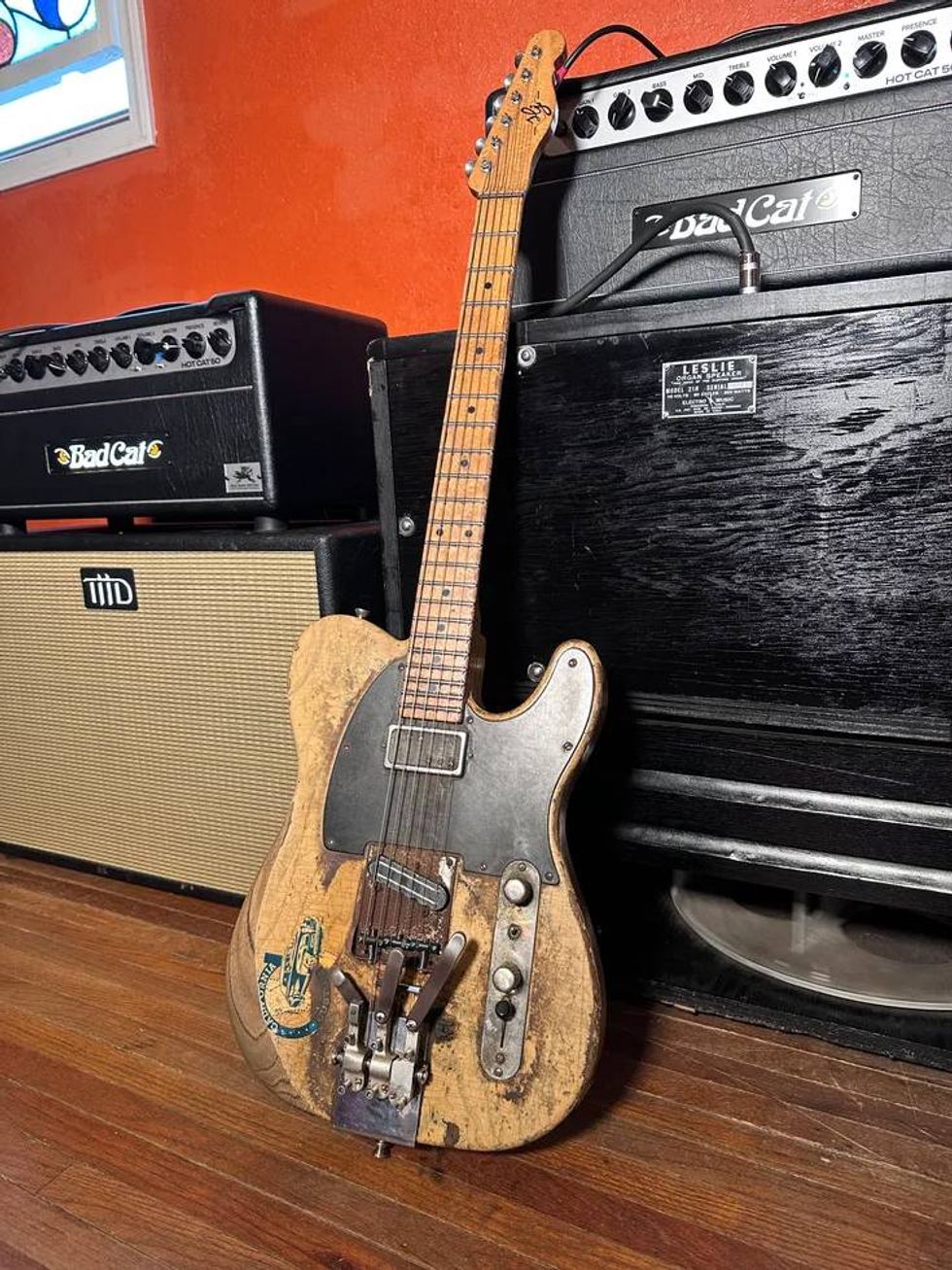 Vintage Telecaster guitar with worn finish, placed near amplifiers and a wooden floor.