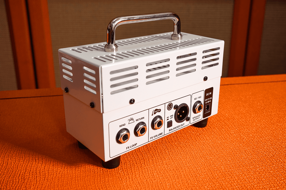White compact amplifier with connections on the back, set on an orange surface.
