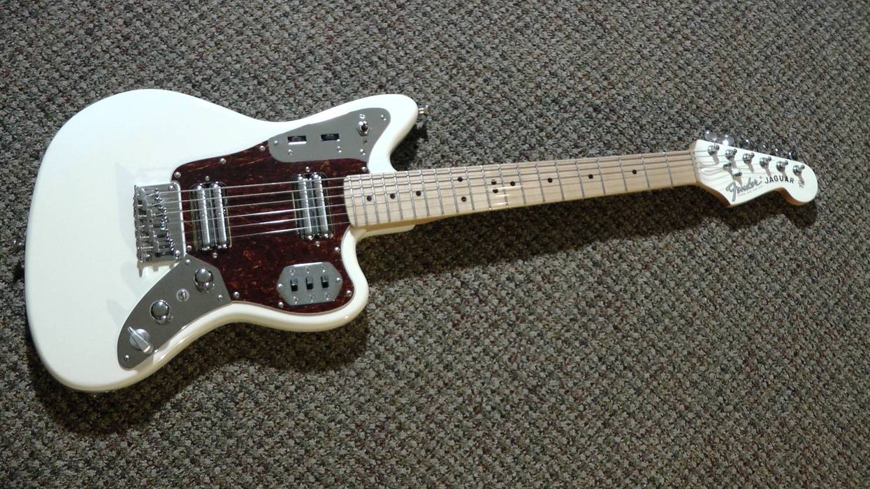 White Fender Jaguar guitar with a tortoiseshell pickguard and maple neck on a carpeted surface.