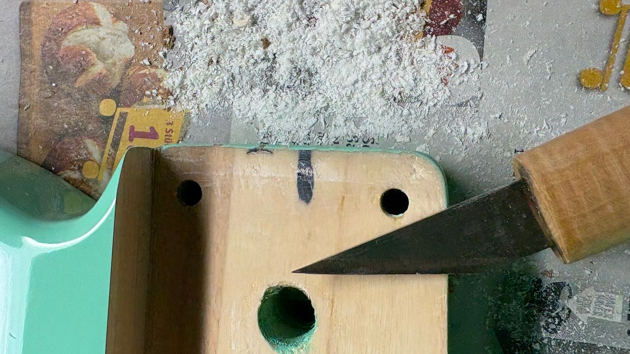 Wood shavings on newspaper next to a green wooden block and a knife cutting into it.