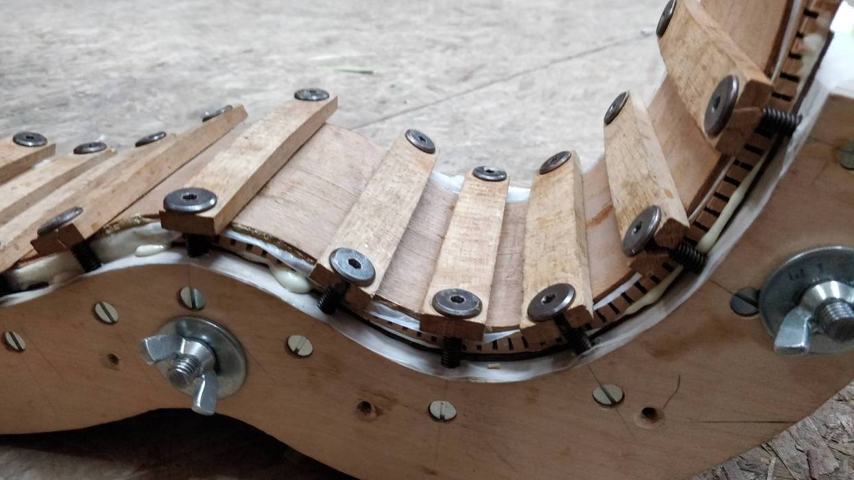 Wooden mechanical component with curved segments and metal fasteners, resting on a surface.