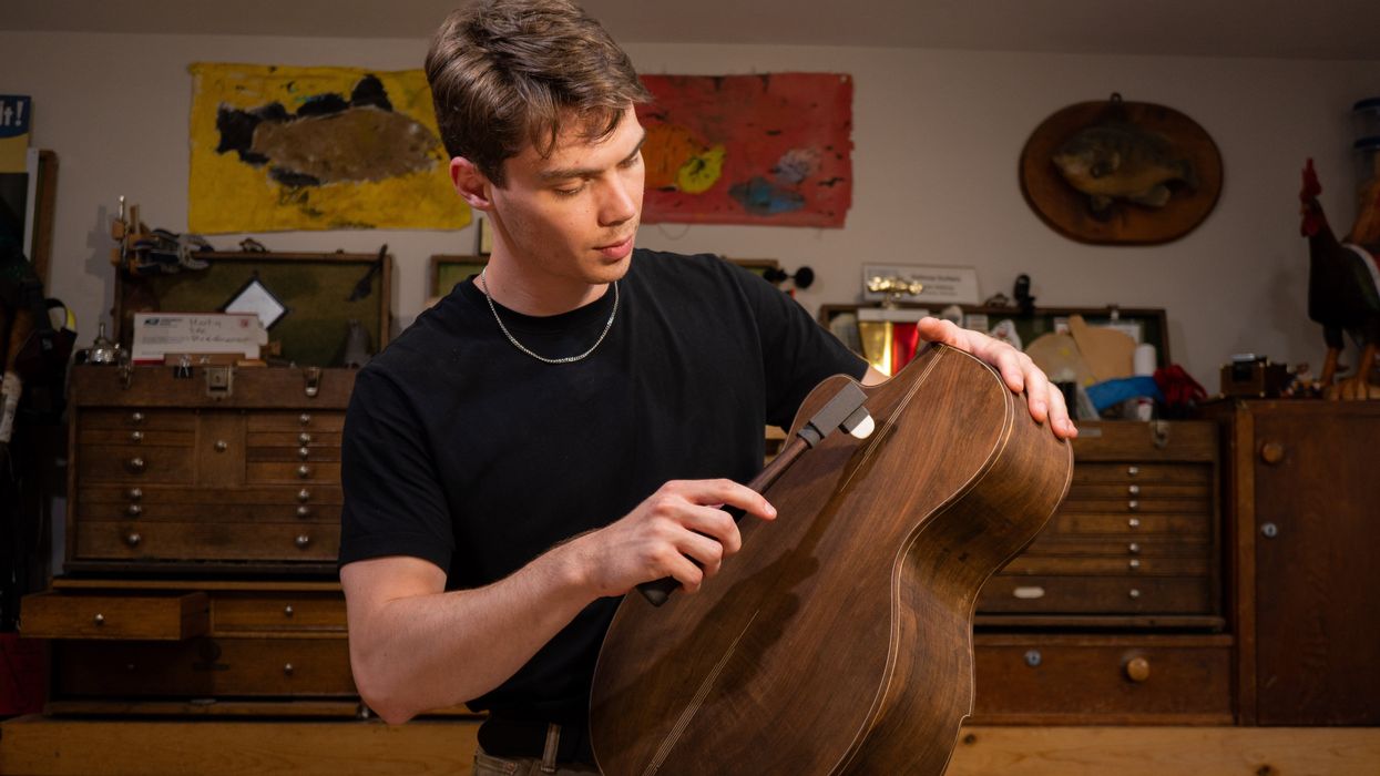 Young man carefully shapes a wooden guitar body in a workshop.